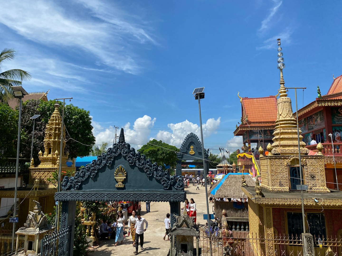 People walk through an ornate temple gateway under blue skies.