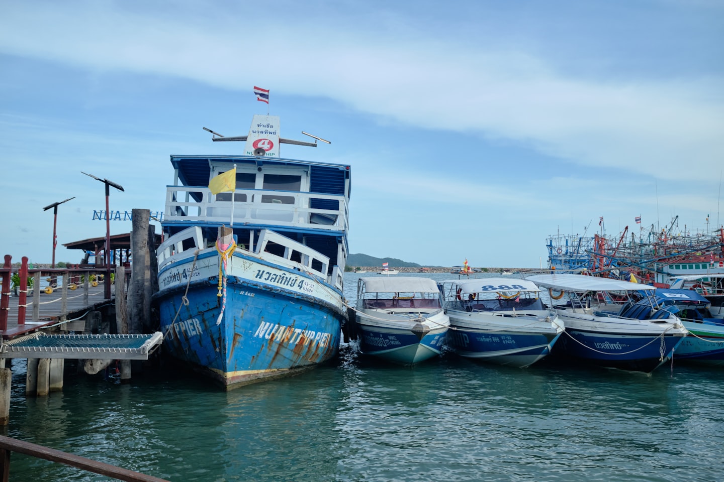 Boats are docked at a wooden pier near green hills.