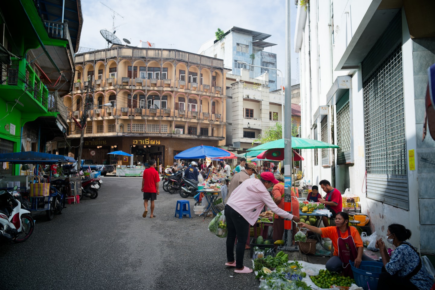 People shop at outdoor market stalls on a busy street.
