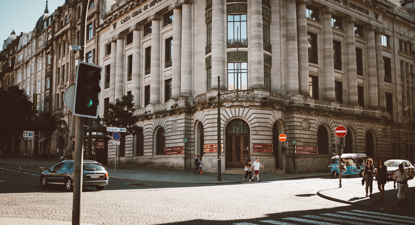 Pedestrians walk past a grand stone building on a city street.