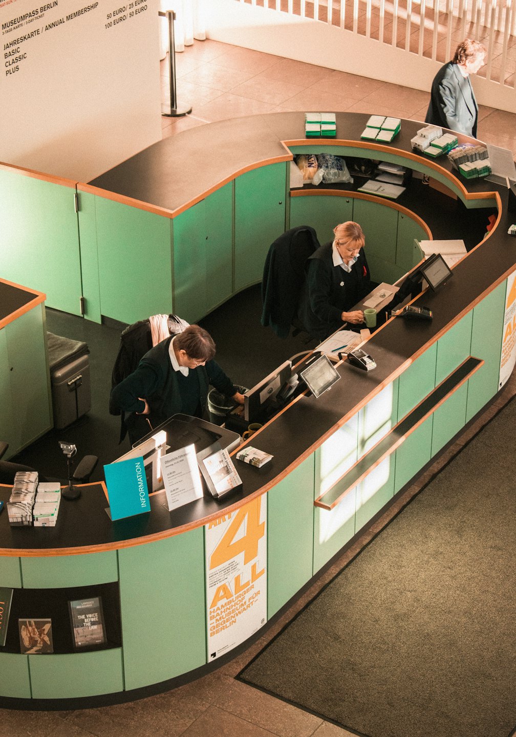 Two women working at a museum information desk with a computer.