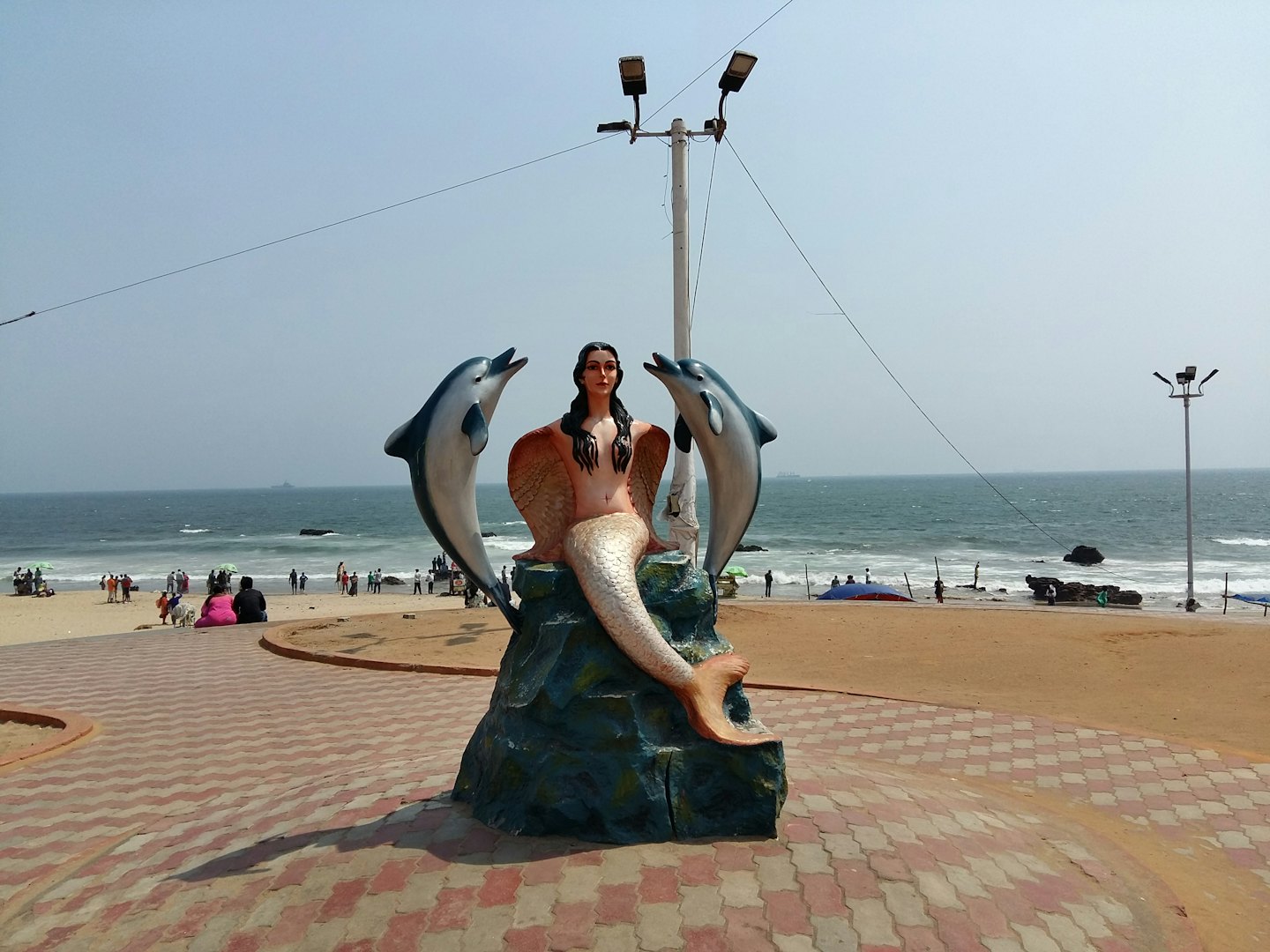 Mermaid and dolphin statue on a coastal stone promenade.
