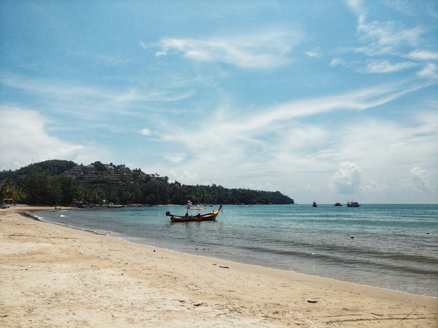 A traditional longtail boat floats on turquoise water near the shore.